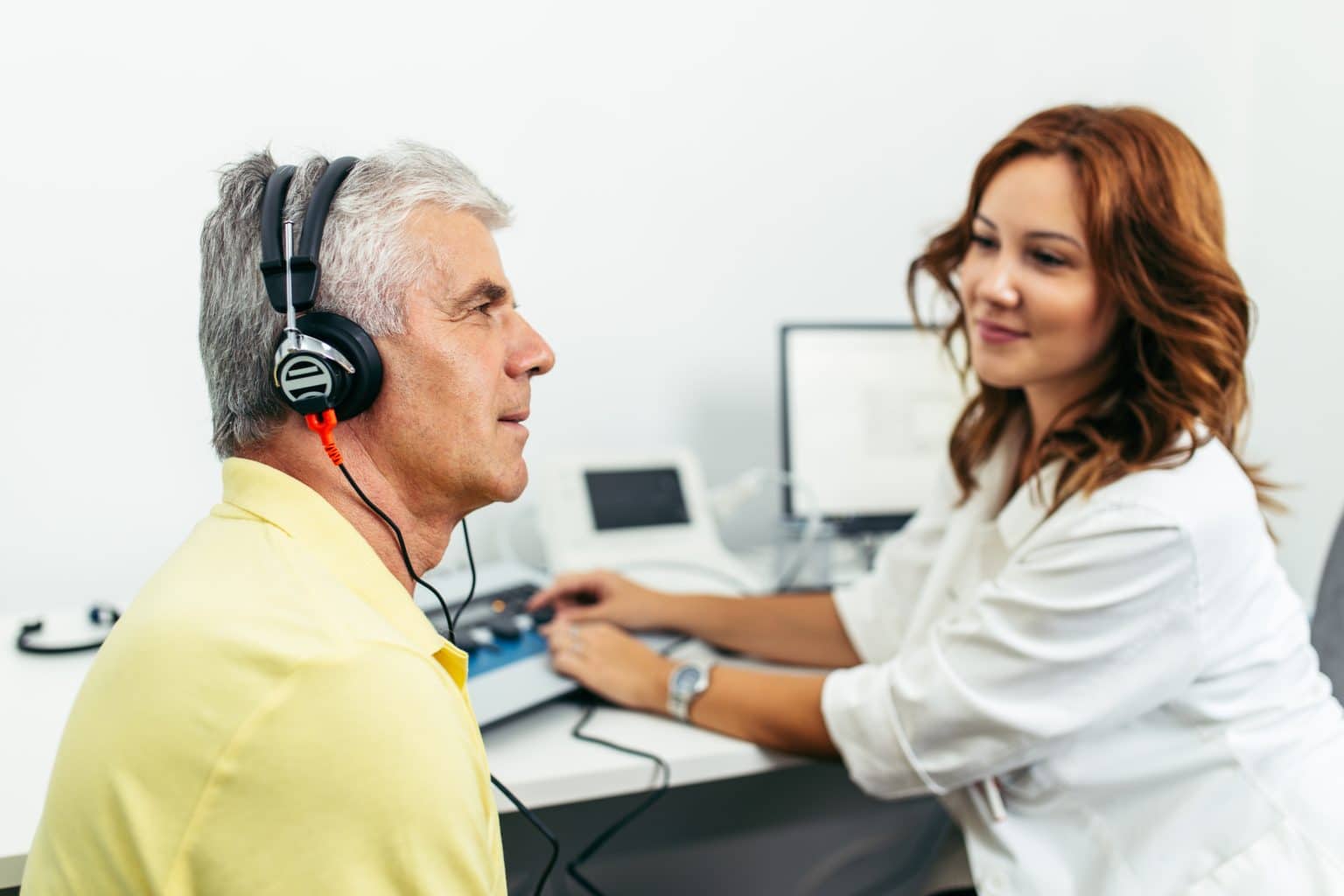 Patient with headphones on gets tested for hearing loss by an audiologist